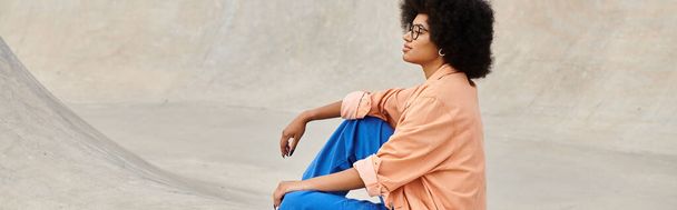 Młoda Afroamerykanka z kręconymi włosami pewnie siedzi na deskorolce w tętniącym życiem miejskim skateparku. - Zdjęcie, obraz