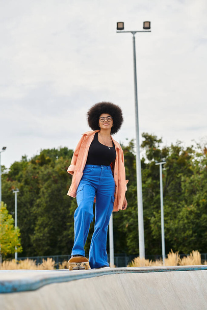 Afroamerykanka z kręconymi włosami na deskorolce na rampie w skateparku. - Zdjęcie, obraz