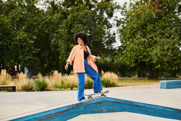 Młoda Afroamerykanka z kręconymi włosami jeździ na deskorolce na rampie w skate parku, wykonując śmiałe triki. - Zdjęcie, obraz