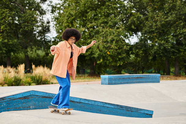 A young African American woman with curly hair fearlessly rides a skateboard on top of a ramp in a vibrant skate park. - Photo, Image