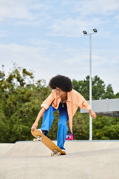 Una joven afroamericana con el pelo rizado haciendo un truco impresionante en su monopatín en un parque de skate. - Foto, imagen