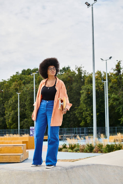 Młoda Afroamerykanka z kręconymi włosami pewnie stoi na rampie na deskorolce w skateparku, gotowa do kolejnego ruchu. - Zdjęcie, obraz