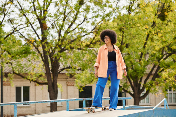 Young African American woman with curly hair skillfully riding a skateboard on top of a ramp at an outdoor skate park. - Photo, Image