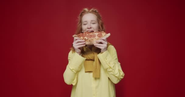 Πεινασμένη νεαρή γυναίκα τρώει νόστιμη πίτσα και απολαμβάνει το φαγητό στο κόκκινο φόντο. Χαρούμενη γυναικεία μπουκιά φρέσκιας ιταλικής πίτσας. Έννοια γρήγορου φαγητού - Πλάνα, βίντεο