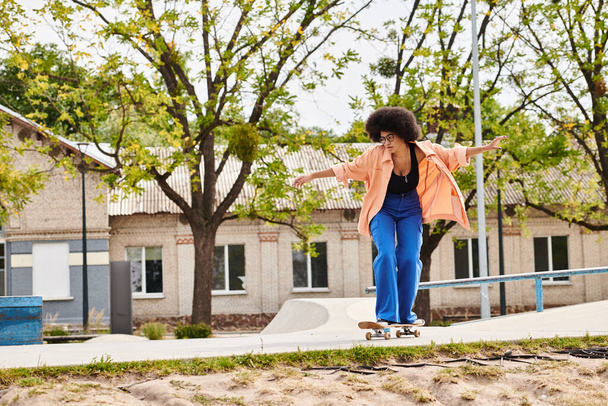 A young African American woman with curly hair gracefully rides a skateboard down a sidewalk in a skate park. - Photo, Image