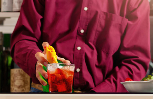 Közelkép egy férfi kezeiről, amint egy vibráló vörös koktélt kevernek egy bárban egy szódavízzel.. - Fotó, kép