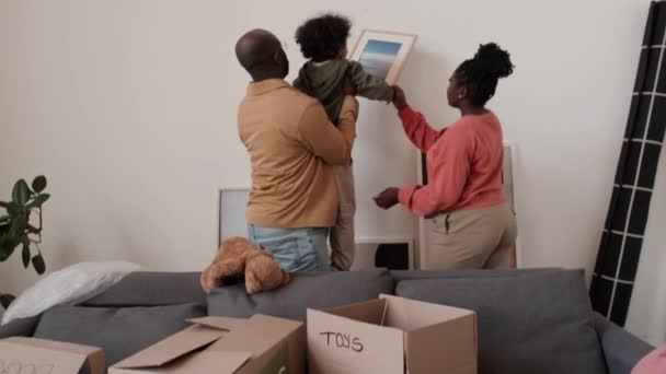 Afro-Amerikaanse ouders houden kleine jongen opknoping foto op muur in nieuw huis na het verhuizen in - Video