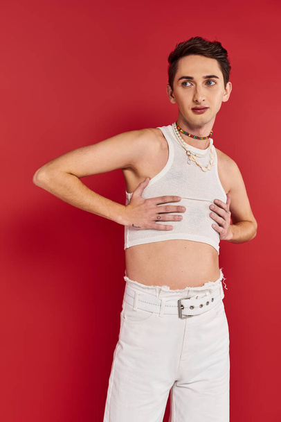 привлекательный модный гей в повседневной одежде с аксессуарами на красном фоне и отводя взгляд - Фото, изображение