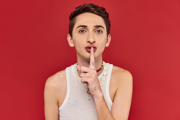 handsome androgynous man with stylish accessories showing silence gesture and looking at camera - Fotoğraf, Görsel
