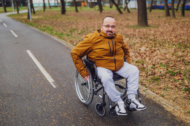 Tyytyväinen halvaantunut mies pyörätuolissa puistossa. Hän liikkuu polkua pitkin.. - Valokuva, kuva