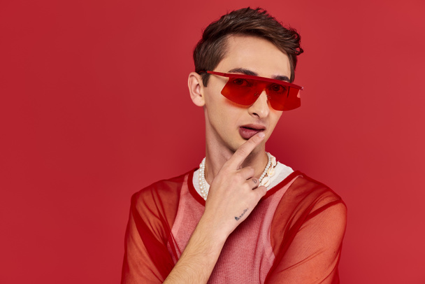 good looking modish androgynous man with red stylish fishnet and sunglasses looking at camera - Photo, Image