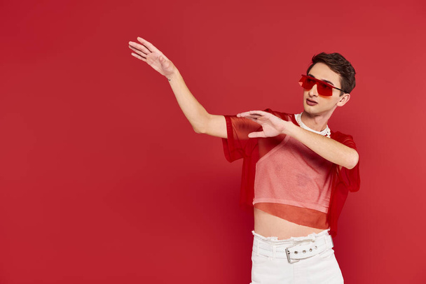 goed geklede androgyne man met rode stijlvolle visnet en zonnebril poseren en wegkijken - Foto, afbeelding