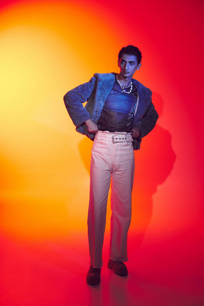 alluring modish androgynous man in purple faux fur posing on vibrant backdrop and looking away - Foto, Imagem