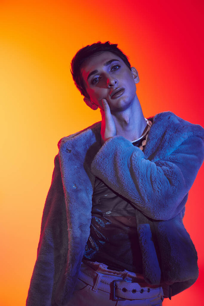 sophisticated androgynous man in purple faux fur posing on vibrant backdrop and looking at camera - Foto, Imagem