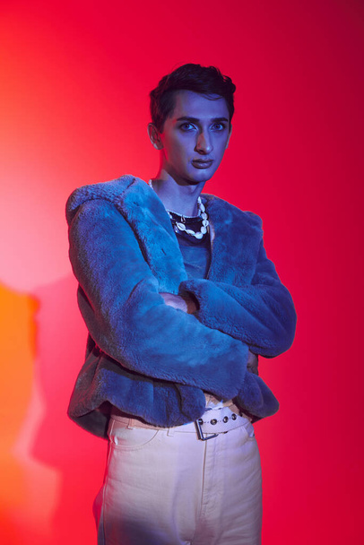well-dressed androgynous man in purple faux fur posing on vibrant backdrop and looking at camera - Фото, зображення