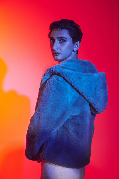 well-dressed androgynous man in purple faux fur posing on vibrant backdrop and looking at camera - Foto, immagini