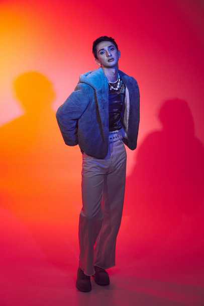divatos androgén férfi lila műszőrme pózol élénk háttér és nézi a kamera - Fotó, kép