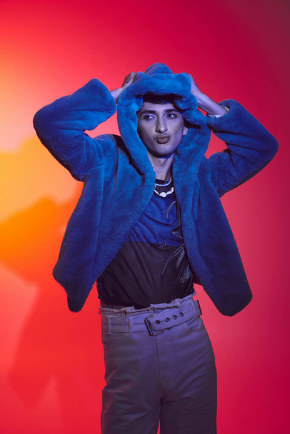 gut aussehender stilvoller schwuler Mann in modischem lila Kunstpelz vor lebendiger Kulisse und wegschauen - Foto, Bild