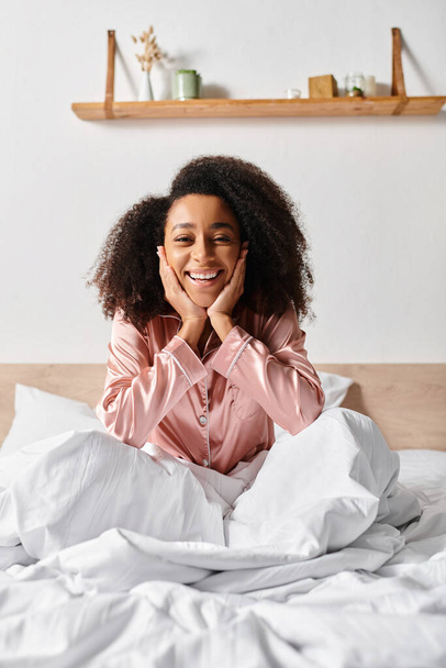 Kręcone Afroamerykanka kobieta w piżamie relaks na białym łóżku pokryte prześcieradłem rano. - Zdjęcie, obraz