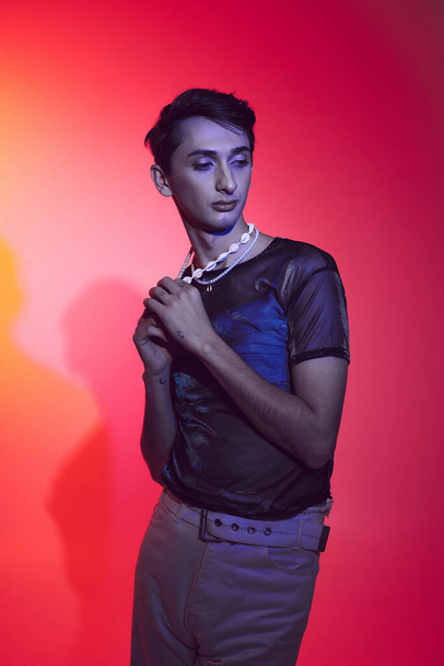 atractivo elegante gay hombre en casual acogedor atuendo posando en vibrante fondo y mirando hacia otro lado - Foto, imagen