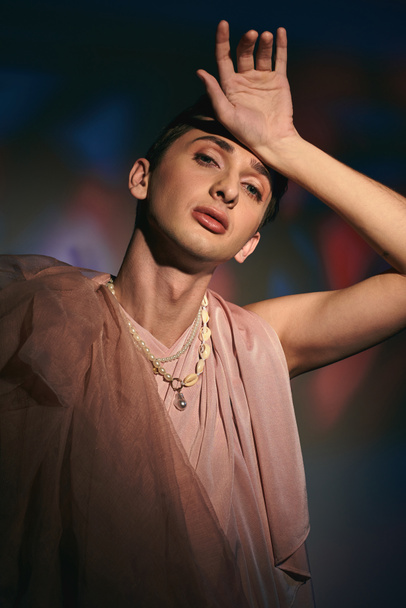 fancy androgynous fashionista with dark hair in pastel attire looking at camera on vivid backdrop - Fotó, kép