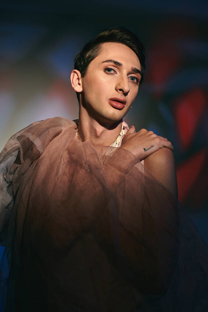 lákavá androgynní móda s tmavými vlasy v pastelových šatech při pohledu na kameru na živém pozadí - Fotografie, Obrázek