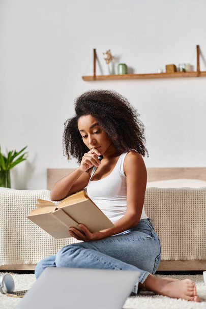 Mujer afroamericana rizada en una camiseta sin mangas se sienta en el suelo absorta en un libro, encontrando la paz en su momento tranquilo. - Foto, imagen