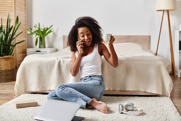 Askılı tişörtlü kıvırcık Afrikalı Amerikalı kadın, modern bir yatak odasında telefon konuşmasına daldı.. - Fotoğraf, Görsel