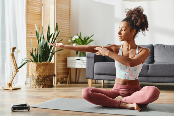 Een krullende Afro-Amerikaanse vrouw in activewear oefent yoga in een serene woonkamer instelling. - Foto, afbeelding