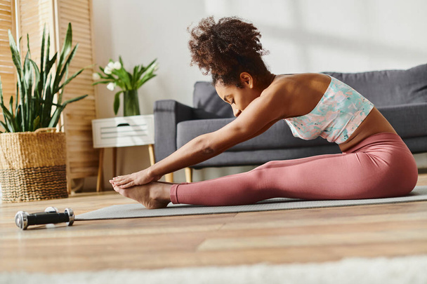Uma mulher afro-americana encaracolada em trajes atléticos pratica ioga no chão, exalando calma e concentração. - Foto, Imagem