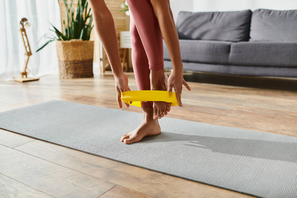 cropped African American woman on yoga mat holding yellow elastics in home workout session. - Photo, Image