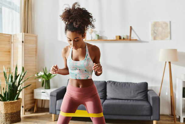 Kıvırcık Afrikalı Amerikalı kadın spor sutyen ve tayt giymiş evde egzersiz yapıyor, gücünü ve bağlılığını gösteriyor.. - Fotoğraf, Görsel