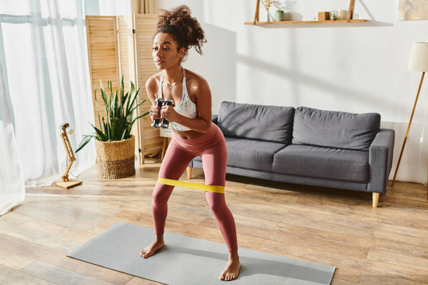Aktif kıyafetli kıvırcık Afrikalı Amerikalı kadın evdeki mindere yoga pozu veriyor.. - Fotoğraf, Görsel