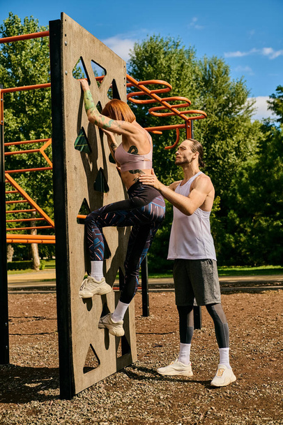 Una mujer decidida, en ropa deportiva, escalando una pared de roca al aire libre con entrenador personal, mostrando motivación y trabajo en equipo. - Foto, Imagen