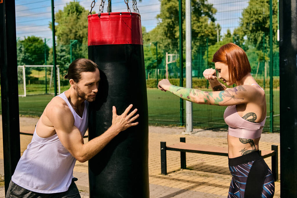 Une femme en tenue de sport s'entraîne à la boxe dans un parc, guidée par un entraîneur personnel, faisant preuve de détermination et de motivation.. - Photo, image