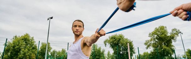 A man wearing sportswear, holding a blue resistance band outdoors. - Photo, Image