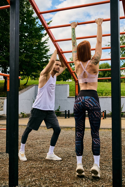 A determined woman, in sportswear, execute pull-ups side by side with a personal trainer outdoors. - Photo, Image