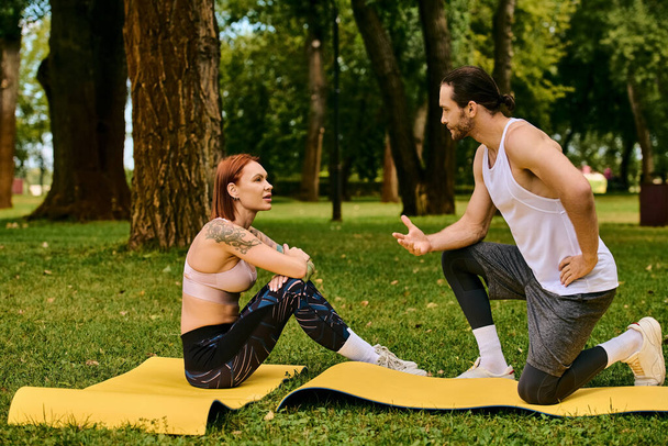 Een man en vrouw in sportkleding op yogamatten in een park, begeleid door een personal trainer. - Foto, afbeelding