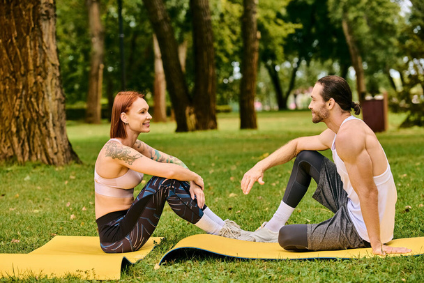 Un en vêtements de sport assis sur un tapis dans le parc, dirigé par un entraîneur personnel, affichant détermination et motivation. - Photo, image