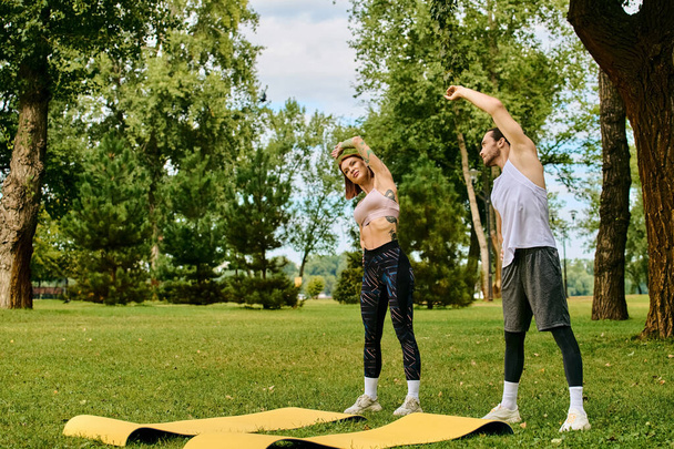 A determined man and woman, both in sportswear, practice in a serene park setting, under the guidance of a personal trainer. - Photo, Image
