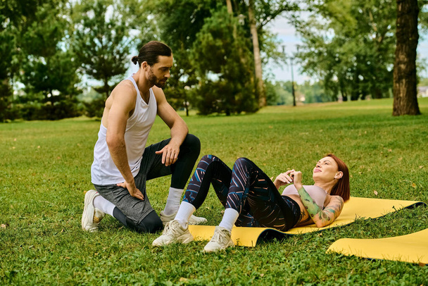 Uma mulher sportswear em um tapete amarelo ao ar livre, guiado por seu personal trainer em uma sessão de ioga cheia de determinação e motivação. - Foto, Imagem