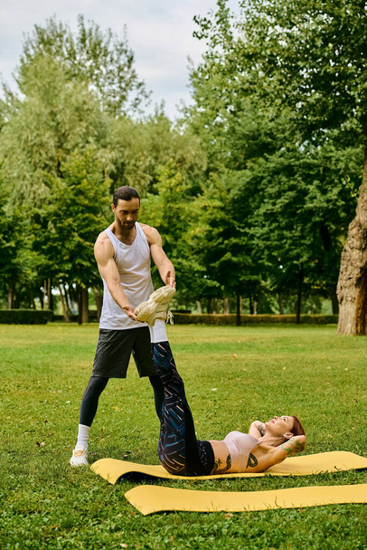 Un homme déterminé se tient au-dessus d'une femme alors qu'elle fait de l'exercice sur un tapis jaune à l'extérieur. L'entraîneur personnel motive et guide la femme. - Photo, image