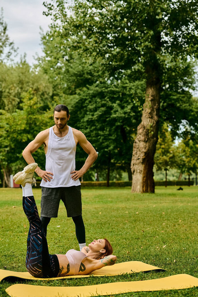 Eine Frau in Sportbekleidung übt unter Anleitung eines Personal Trainers zielstrebig und motiviert Yoga in einem ruhigen Park. - Foto, Bild