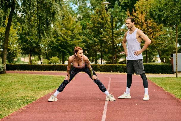A woman in sportswear, guided by their personal trainer, display determination and motivation while stretching outdoors in a serene park setting. - Photo, Image