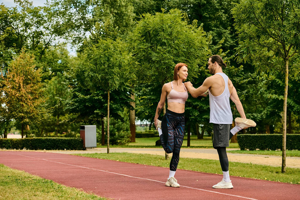 Egy férfi és egy nő a sportruházatban, együtt nyújtózkodnak a park ösvényén. Eltökéltségük és motivációjuk átragyog. - Fotó, kép