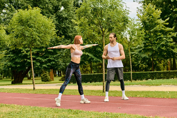 Ένας άνδρας και μια γυναίκα σε αθλητικά ρούχα που εκτείνονται σε εξωτερικούς χώρους, δείχνοντας κίνητρο. - Φωτογραφία, εικόνα