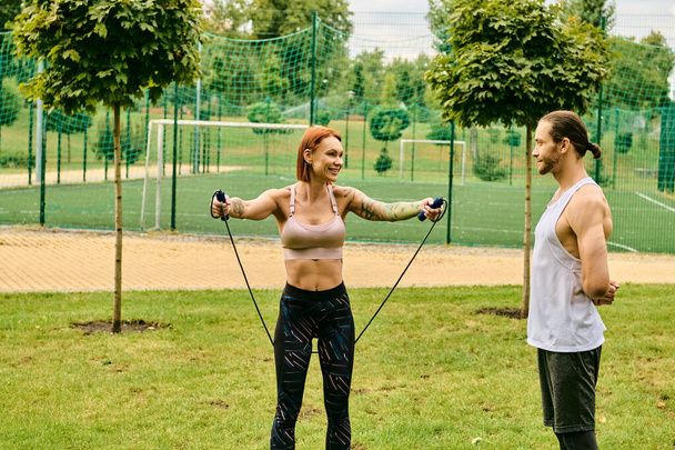 Eine entschlossene Frau in Sportbekleidung trainiert mit einem Personal Trainer in einer lebendigen Parklandschaft. - Foto, Bild