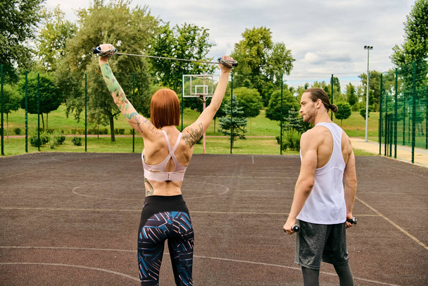 Ένας άνδρας και μια γυναίκα στα αθλητικά, καθοδηγούμενοι από έναν προσωπικό γυμναστή, στέκονται στο γήπεδο με αποφασιστικότητα και κίνητρο.. - Φωτογραφία, εικόνα