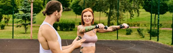 Egy határozott nő melltartóban egy súlyzót tart a szabadban, ami motivációt és erőt mutat egy edzésen, amit egy személyi edző vezet.. - Fotó, kép