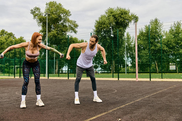 Ένας αποφασισμένος άνδρας και μια γυναίκα στα αθλητικά γυμνάζονται μαζί με αλτήρες έξω - Φωτογραφία, εικόνα